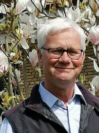 Bild vergrößern: Herr Thole steht vor einem Magnolienbaum, er trägt eine Brille und lächelt in die Kamera.