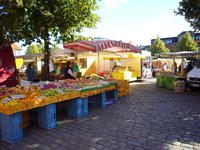 Bild vergrößern: Zu sehen ist der Wochenmarkt an einem sonnigen Tag. Im Vordergrund sind Obstkisten aufgebaut unter einem Sonnenschirm.