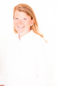 Das Bild zeigt Anja Neumann. Sie trägt schulterlange Haare und eine weiße Bluse vor einem weißen Hintergrund.