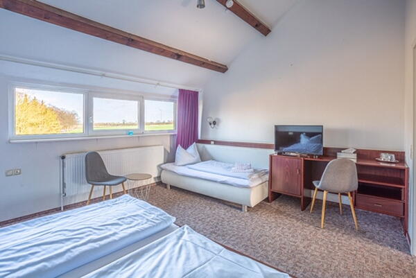 zu sehen ist ein Zimmer, zwei Betten plus Extrabett, Schreibtisch, Stuhl und Bildschirm
