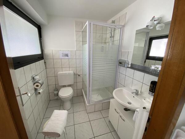 zu sehen ist ein Badezimmer mit Toilette, Dusche und Waschbecken, in Weiß gehalten