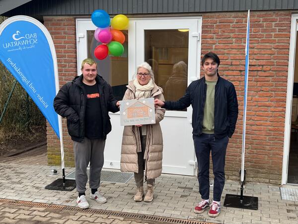 Auf dem Bild sind zu sehen: Cedrik Böhnert, Sigrid Wassermeyer, Philipp Hamkens, alle halten zusammen ein Schild der Schlüsselübergabe hoch.